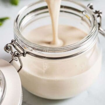 A jar of creamy white sauce being poured inside, with the lid open on a light surface—perfect alongside easy jams and pickles.
