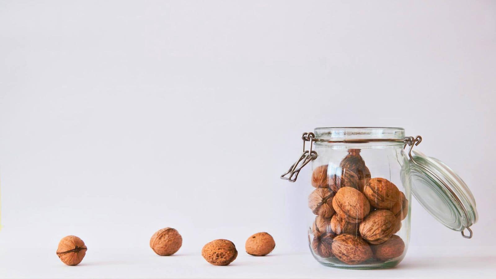 Open jar of walnuts, with four pieces of walnuts on a white background