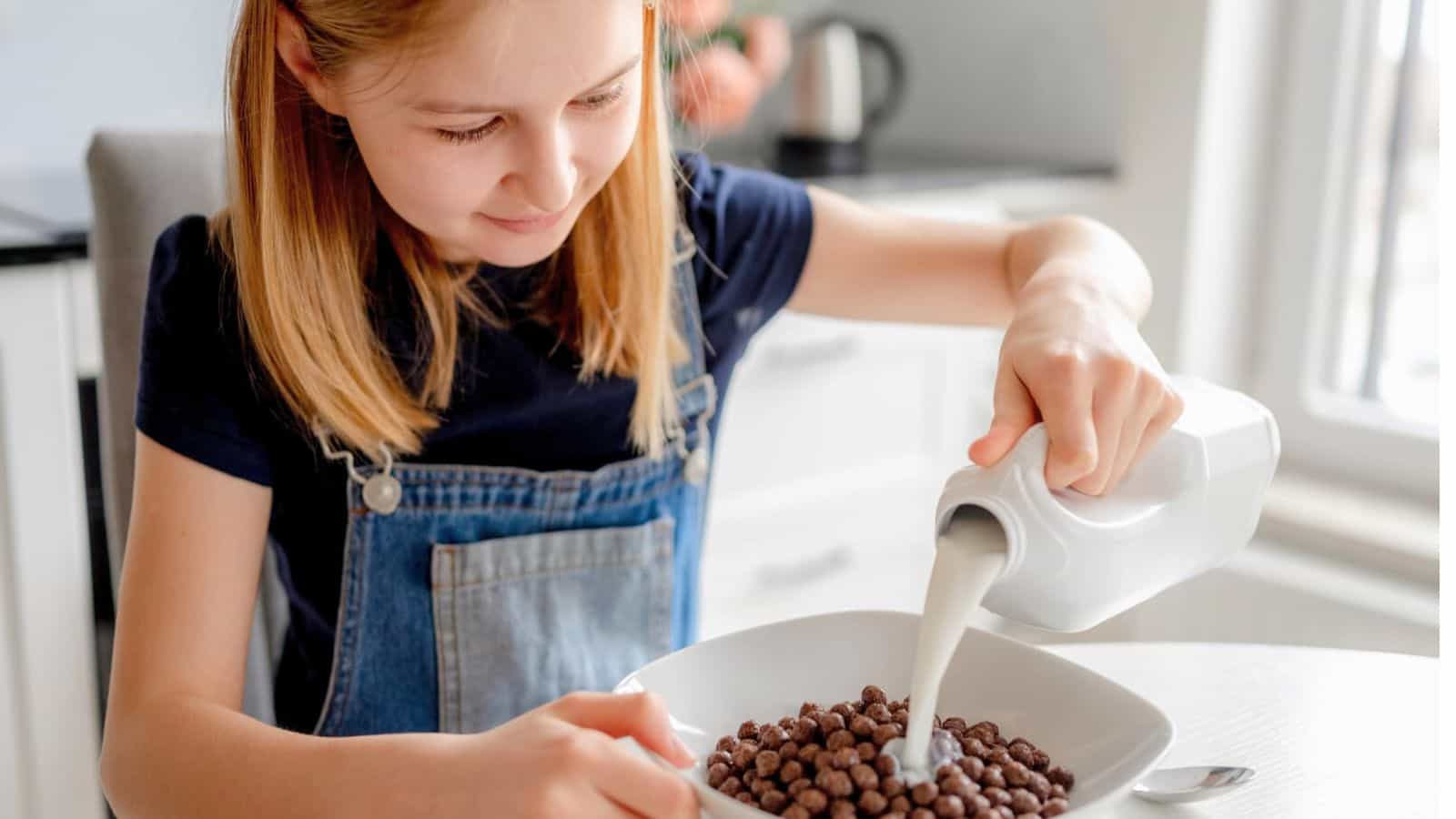 Little girl pouring milk onto her breakfast cereal