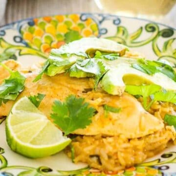 Cilantro lime chicken on a plate next to avocado and cilantro garnish.