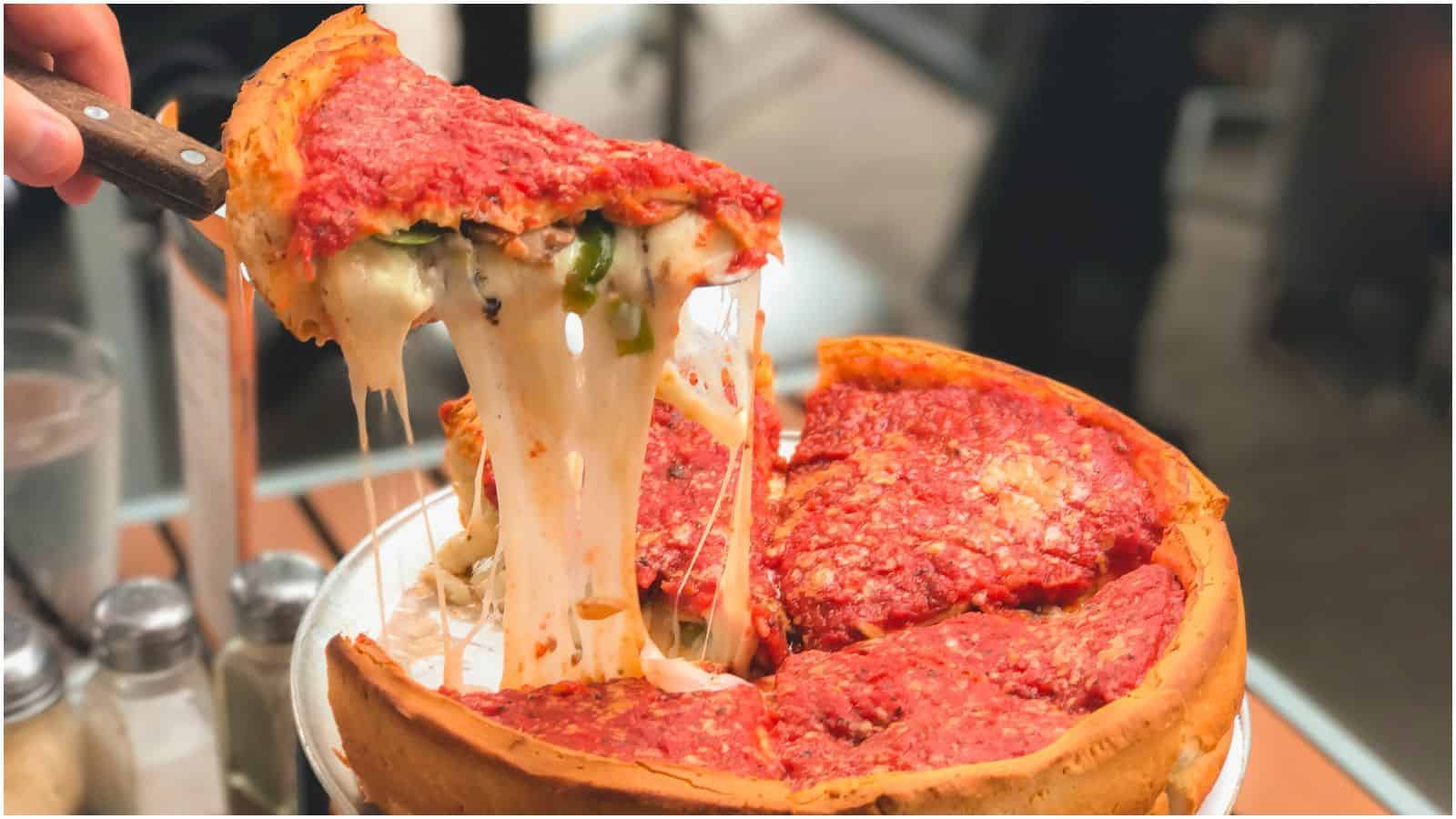 A piece of deep dish pizza being lifted off of the rest of the pizza