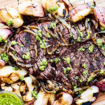 Grilled steak with peaches and onions on a wooden cutting board.