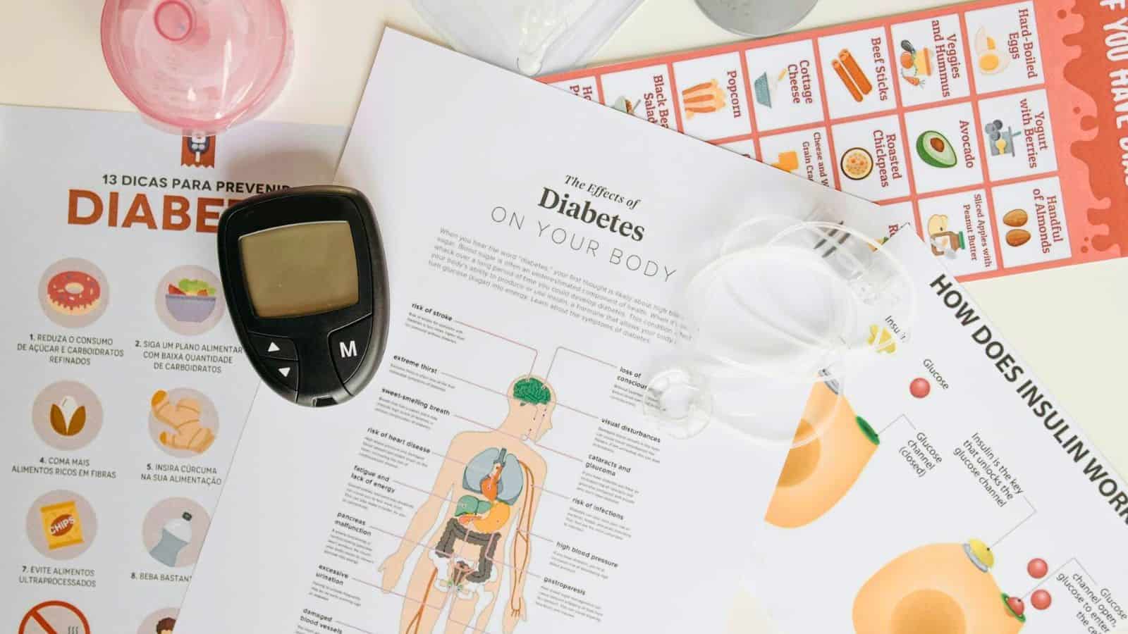 A flat lay of diabetes-related materials, including educational pamphlets, a blood glucose meter, insulin pump tubing, and diagrams explaining the effects of diabetes on the body and how insulin works. Some documents are in both English and Spanish.