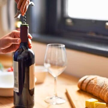 Person uncorking a wine bottle with bread and a wine glass in the background