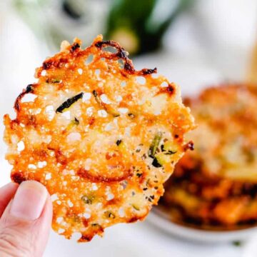 A hand holding a zucchini parmesan chip.