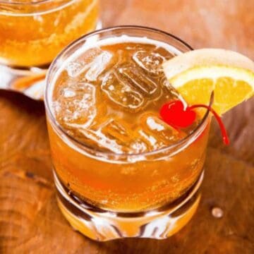 Two amaretto sour cocktails garnished with orange slice and cherries.