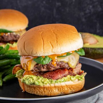 An up-close shot of bacon-avocado ground beef burger on a flat white surface.