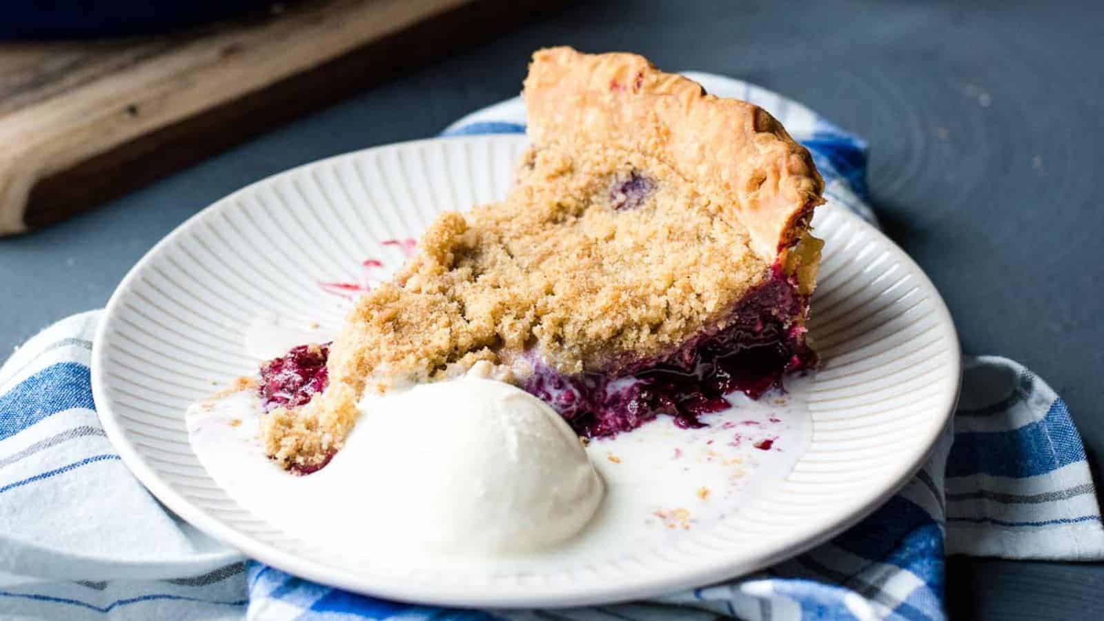 Overhead shot of blackberry crumble pie with one slice on a serving plate.