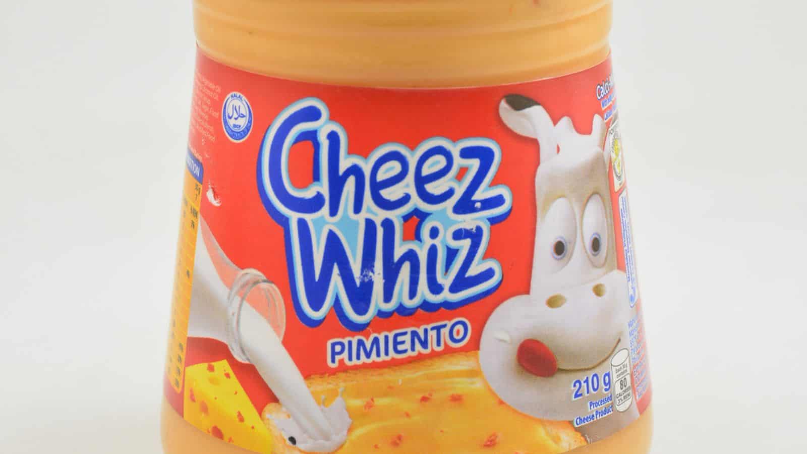 A jar of Cheez Whiz Pimiento, with a 210-gram label, featuring an image of melted cheese being poured and a cartoon cow on the packaging.