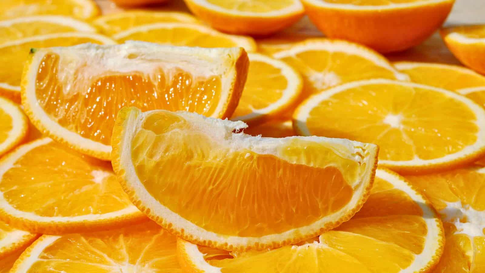 Orange slices are arranged in a layered fashion. Two quarter slices of orange stand out prominently in the foreground, showing juicy and translucent flesh. The background consists of numerous circular orange slices creating a vibrant display of citrus fruit.