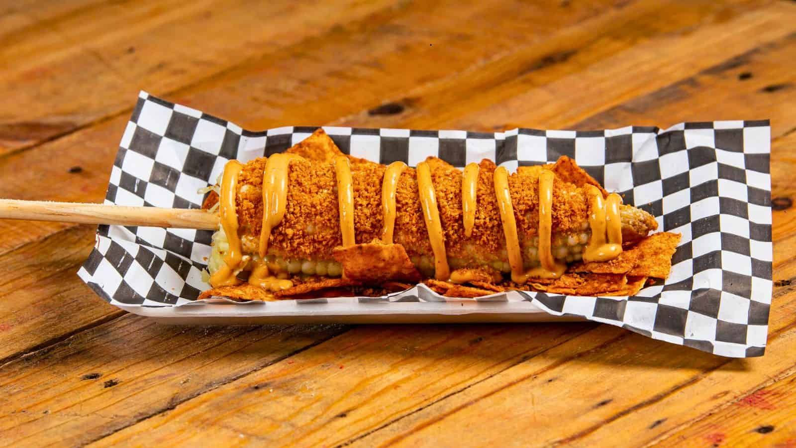 Corn dog on a stick placed on a checkered paper plate