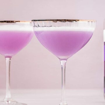 Two empress 1908 gin sours next to a bottle of purple gin.