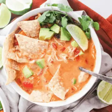 A bowl of chicken tortilla soup with tortilla chips, diced avocado, and sliced lime on top.