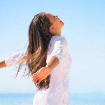 Person raising her arms sidewards with a beach background