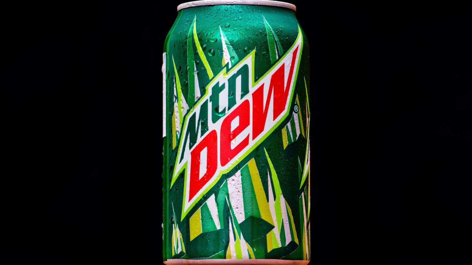 A green can of Mountain Dew is shown against a black background. The can features a stylized logo with the words "mtn dew" and a design of green and dark green stripes. The surface of the can is covered in water droplets.