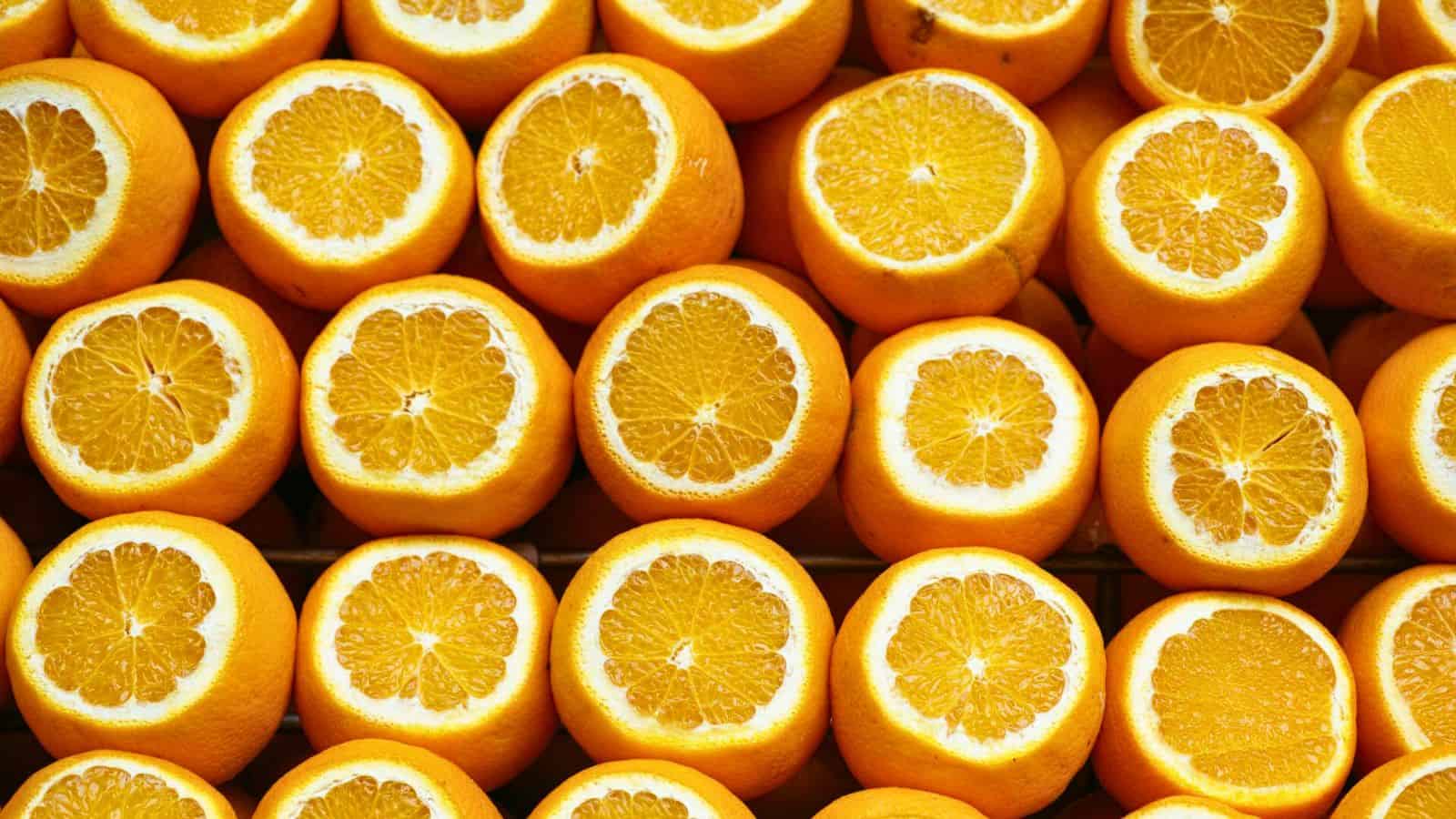 A close-up image of numerous halved oranges displayed in rows. The sections of each orange are clearly visible, showcasing their juicy, vibrant flesh and bright orange peel. The uniform arrangement creates a visually appealing pattern.