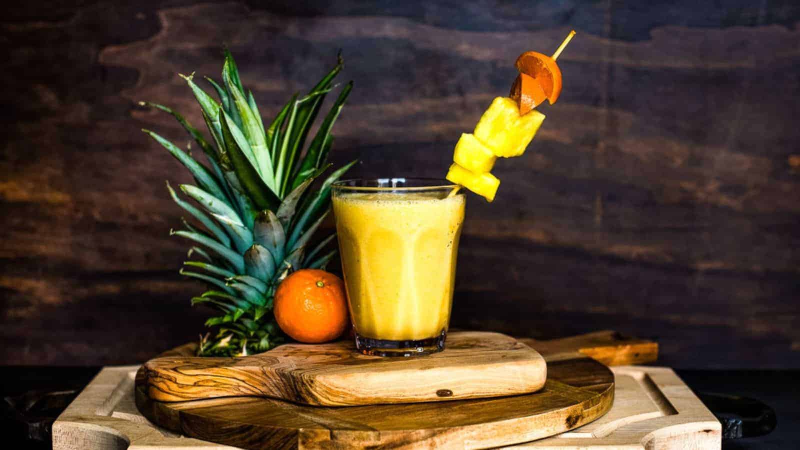 A smoothie in a glass on a stack of cutting boards next to a fresh orange and pineapple top with text overlay.