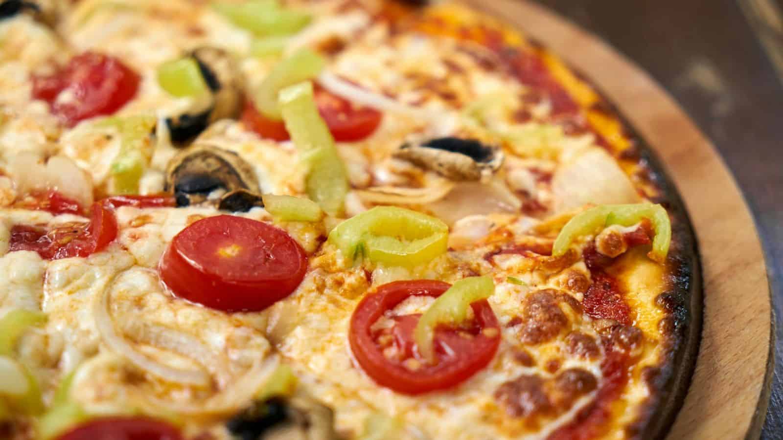 A close-up view of a pizza topped with sliced green bell peppers, cherry tomatoes, mushrooms, and onions on a cheese and tomato base, placed on a wooden surface.