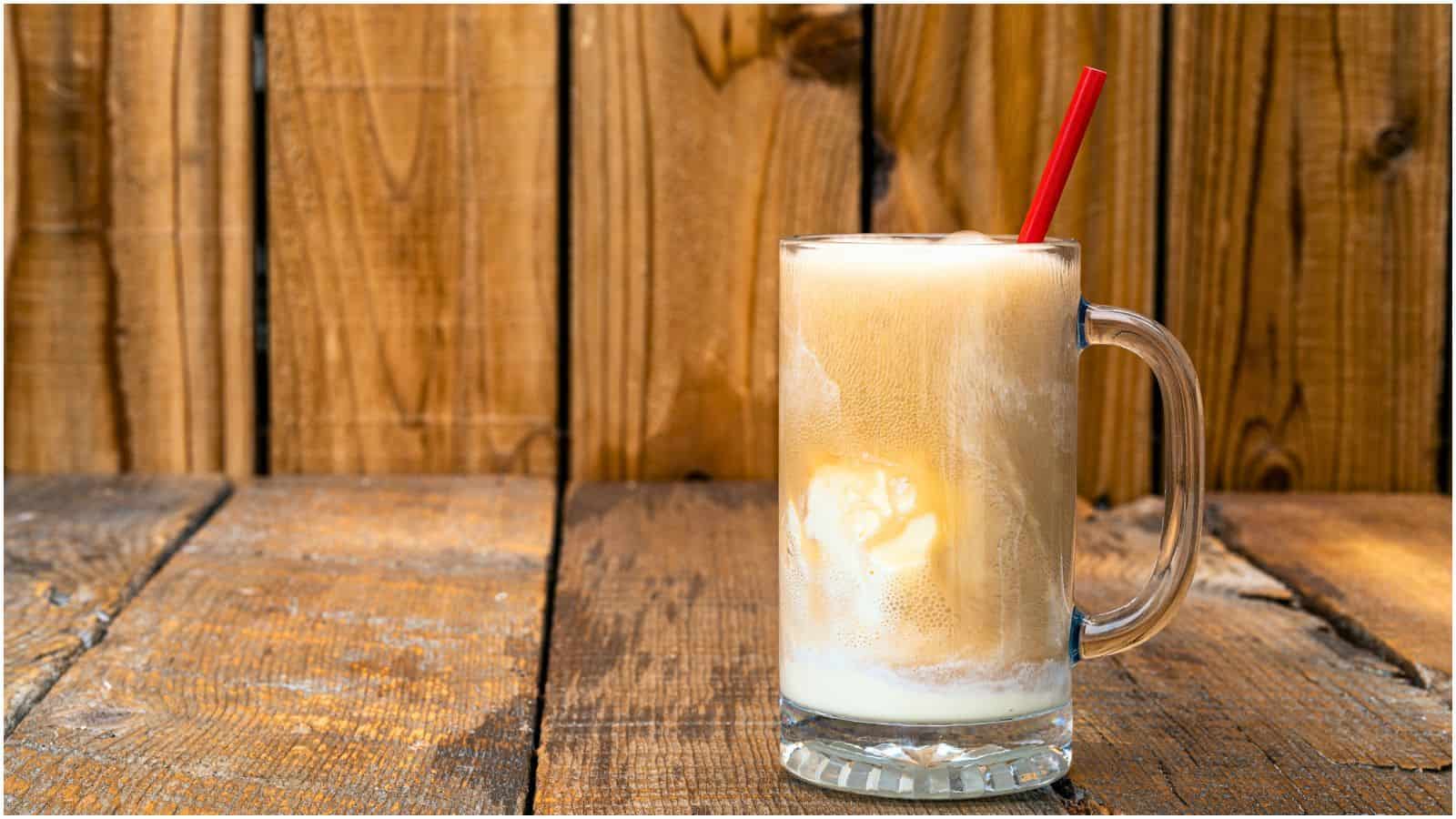 A mug of root beer float with a red straw sits on a wooden surface. The frothy beverage consists of vanilla ice cream and root beer against a background of wooden planks.