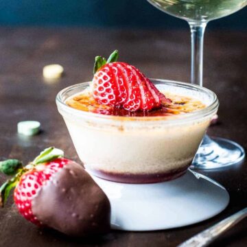 Close up of strawberry crème brûlée next to a glass of champagne.