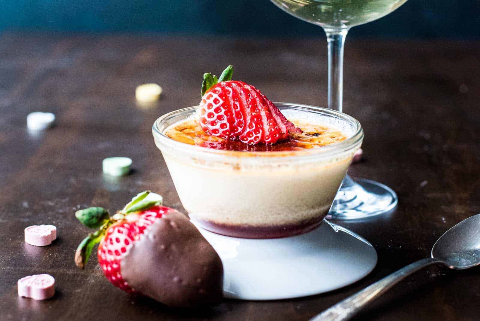 Close up of strawberry crème brûlée next to a glass of champagne.