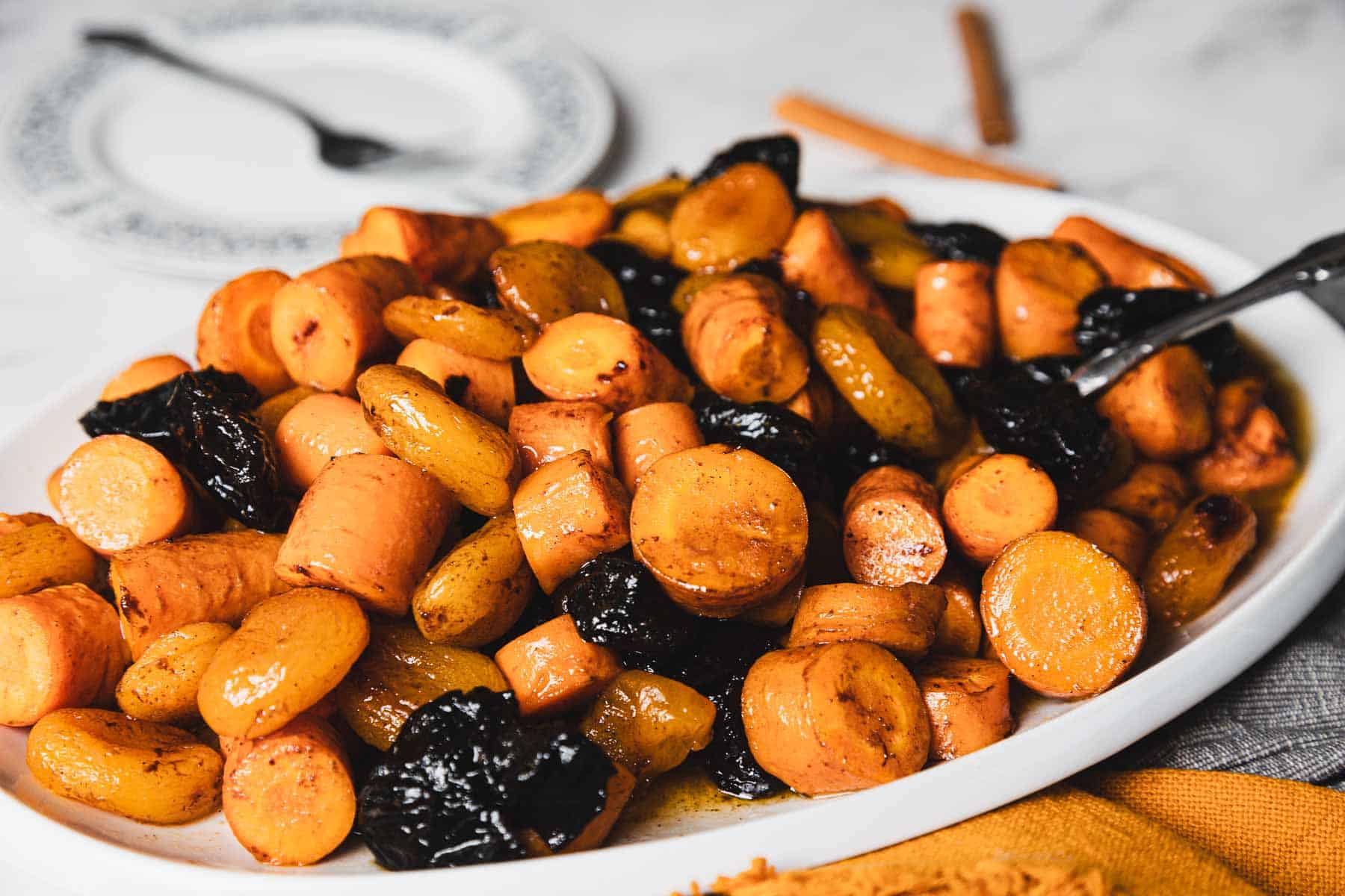 A white plate filled with cooked sliced carrots and prunes, with a fork on the side.