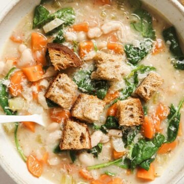 A bowl of white bean soup with carrots and croutons.