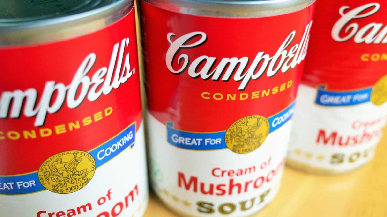 Three cans of Campbell's condensed soup are lined up. The labels display "Cream of Mushroom" in red letters and include a blue section that says "Great for Cooking.