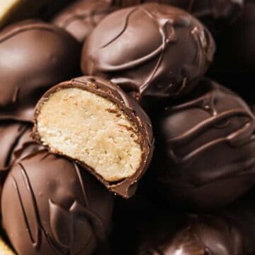 A bowl filled with keto-friendly, chocolate-coated truffles, one cut open to reveal a creamy, light-colored interior. The surface of these delights is decorated with drizzles of chocolate.
