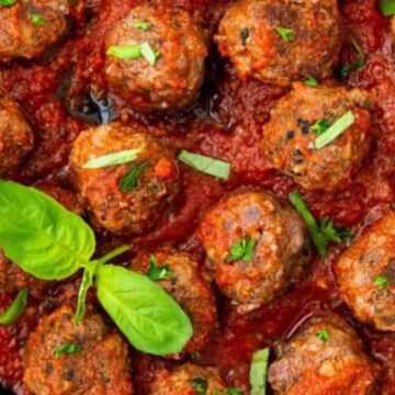 A skillet filled with meatballs in a rich tomato sauce, garnished with fresh basil leaves and chopped parsley.