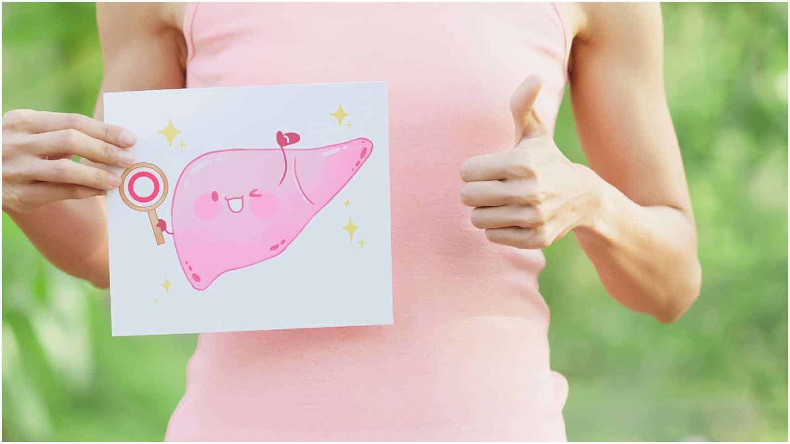 A person in a pink tank top holds a drawing of a smiling pink liver with a checkmark and sparkles, while giving a thumbs-up with their other hand. The background is a blurred natural outdoor setting.