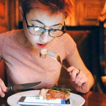 Woman eating steak with her phone in front of her