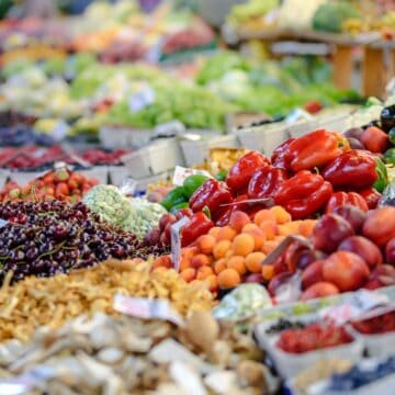 A vibrant farmers' market display showcases a variety of fresh fruits and vegetables. From nutrient-rich mushrooms to underrated apricots, the arrangement features red bell peppers, eggplants, lettuce, and more. Baskets and crates keep these nutritional powerhouses beautifully organized.