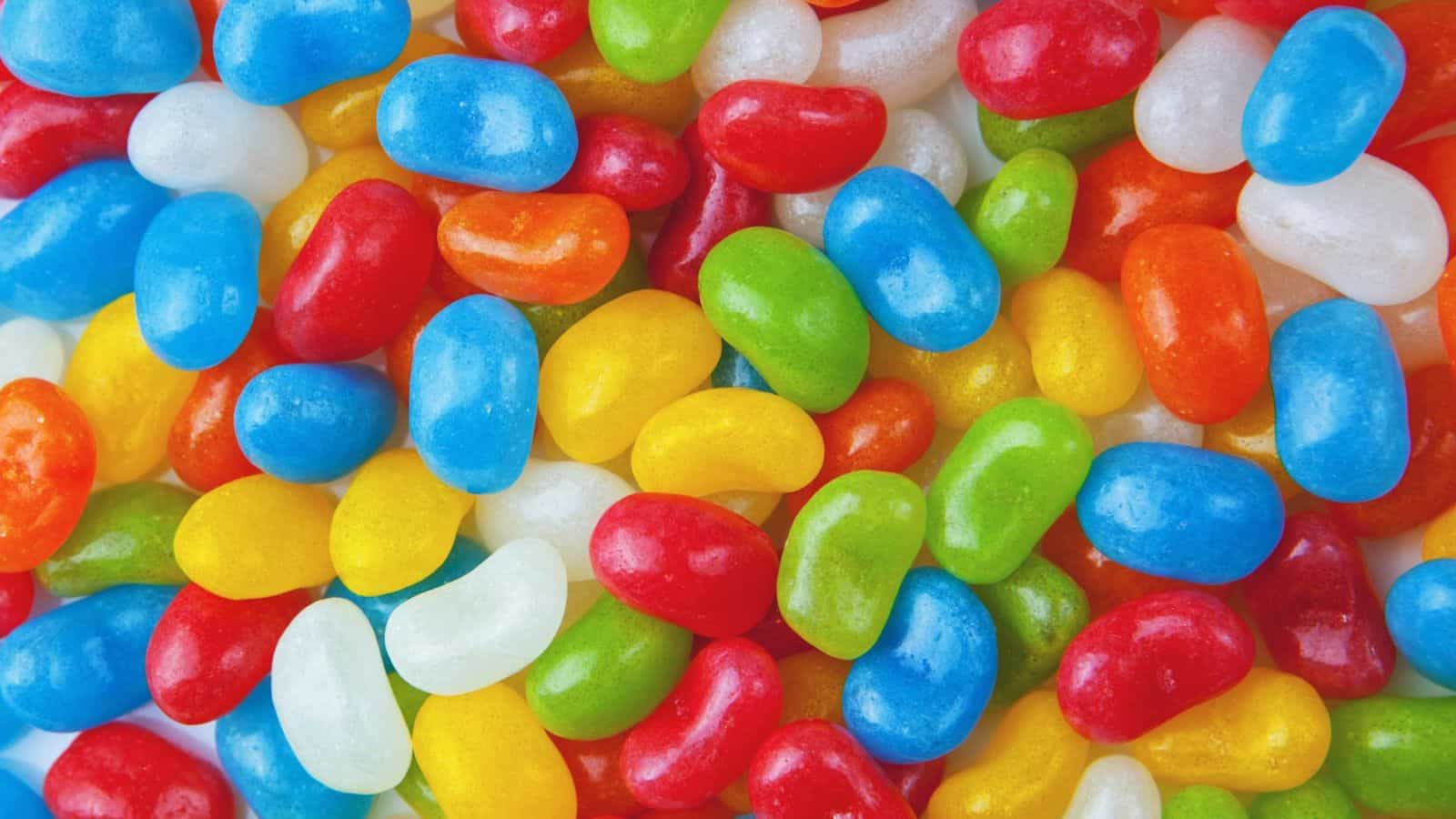 A colorful assortment of jelly beans, including red, blue, green, yellow, orange, and white, fills the image, creating a bright and vibrant pattern.