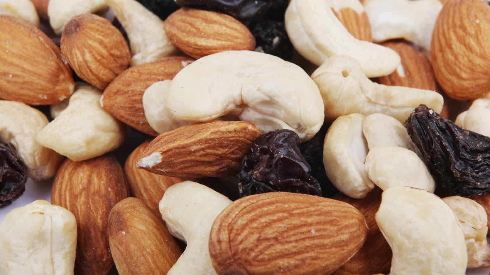 A close-up image of assorted mixed nuts and dried fruit, including almonds, cashews, and raisins. The nuts are mostly whole, and the dried raisins are scattered throughout. The colors range from off-white to dark brown.