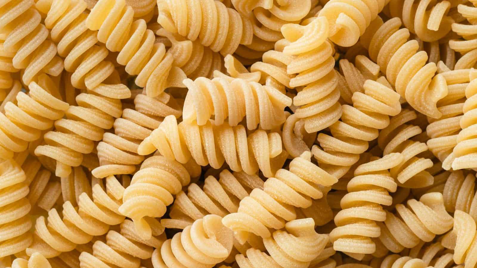Close-up of uncooked, dry rotini pasta. The spiraled pasta pieces are tightly packed together, showcasing their textured surface and pale yellow color.