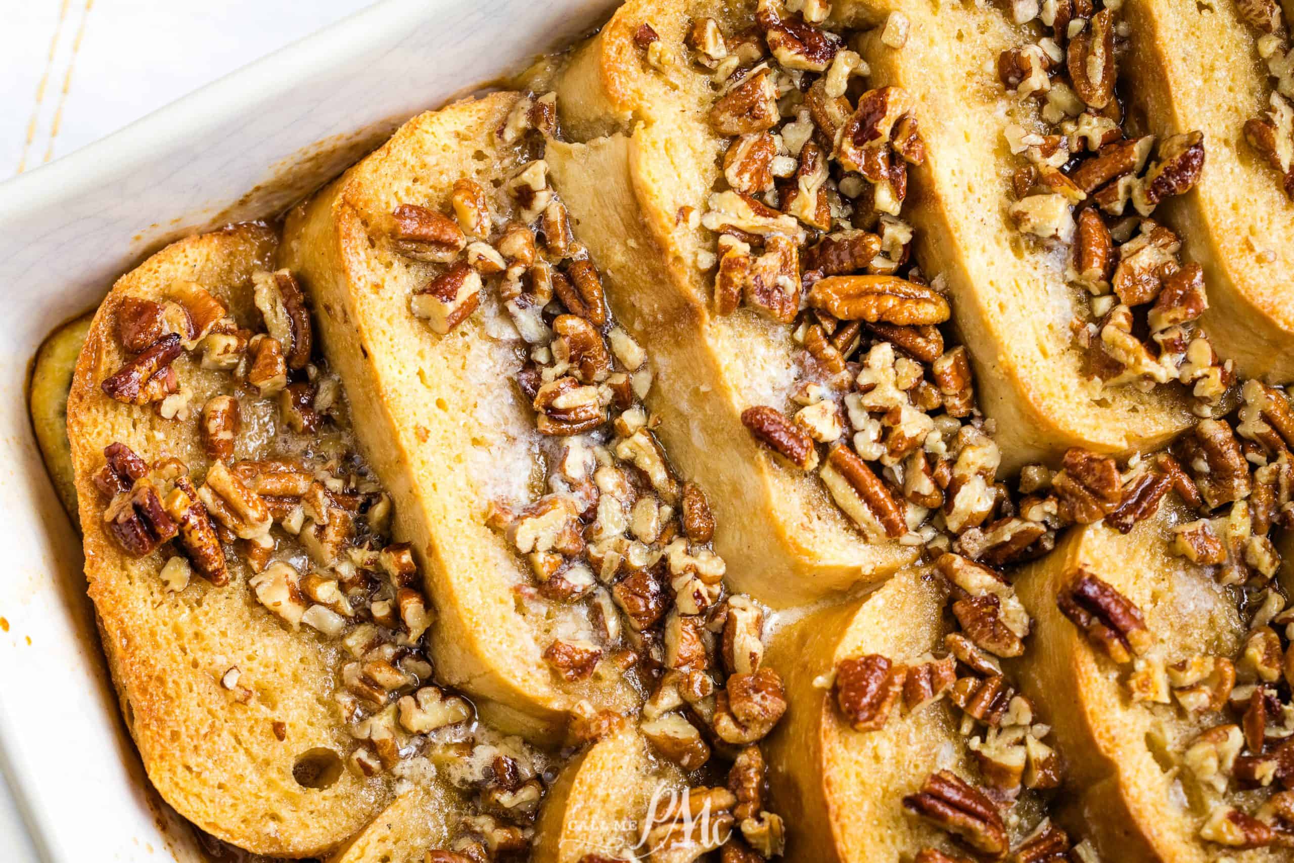 A close-up of a baked dish filled with sliced French bread soaked in a custard mixture and topped with chopped pecans. The bread appears golden brown and slightly crispy, while the nuts add a crunchy texture to this auto draft of culinary perfection.