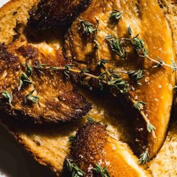 Close-up of a toasted bread slice topped with sauteed Lion's Mane mushrooms and garnished with fresh thyme sprigs. The mushrooms are perfectly browned, and the thyme adds a green contrast to the overall warm tones, making this recipe both visually appealing and deliciously tempting.