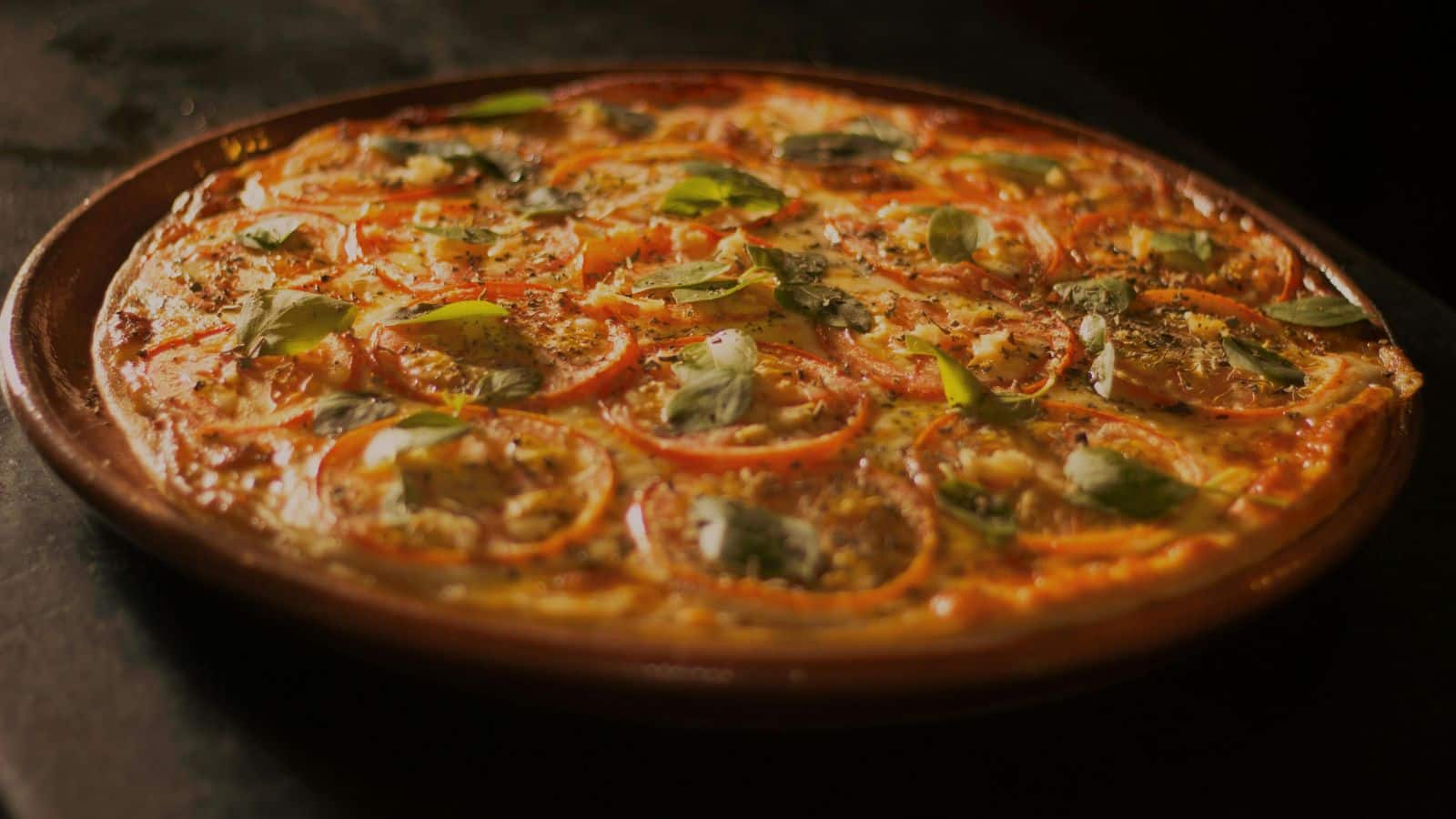 A pizza topped with sliced tomatoes, fresh basil leaves, and melted cheese on a wooden table.