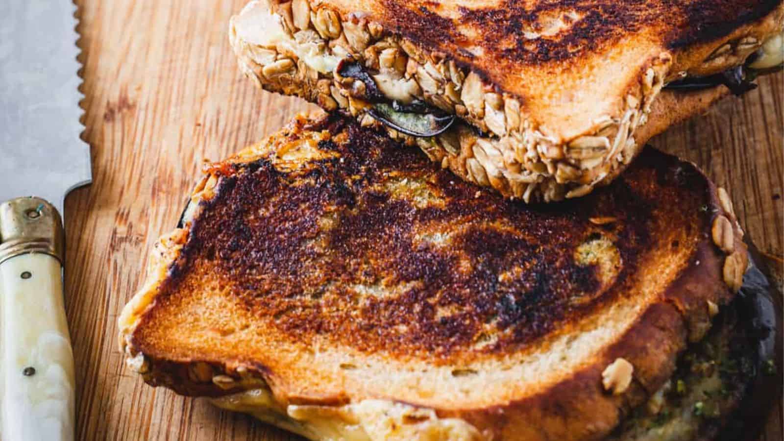 A grilled sandwich with mushrooms, tomatoes and pesto on a cutting board.