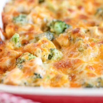 A close-up of a baked casserole in a red dish, featuring melted cheese, broccoli, and pieces of chicken. The dish has a golden-brown crust, indicating it's fully cooked.