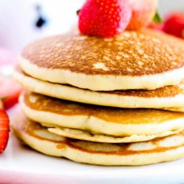 A stack of three fluffy pancakes topped with halved strawberries on a white plate offers a delightful breakfast scene. Just as Auto Draft in web applications automatically saves your work, these pancakes deliver consistent satisfaction. Additional sliced strawberries enhance the setting's charm.
