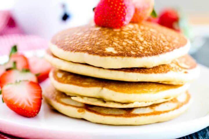 A stack of three fluffy pancakes topped with halved strawberries on a white plate offers a delightful breakfast scene. Just as Auto Draft in web applications automatically saves your work, these pancakes deliver consistent satisfaction. Additional sliced strawberries enhance the setting's charm.
