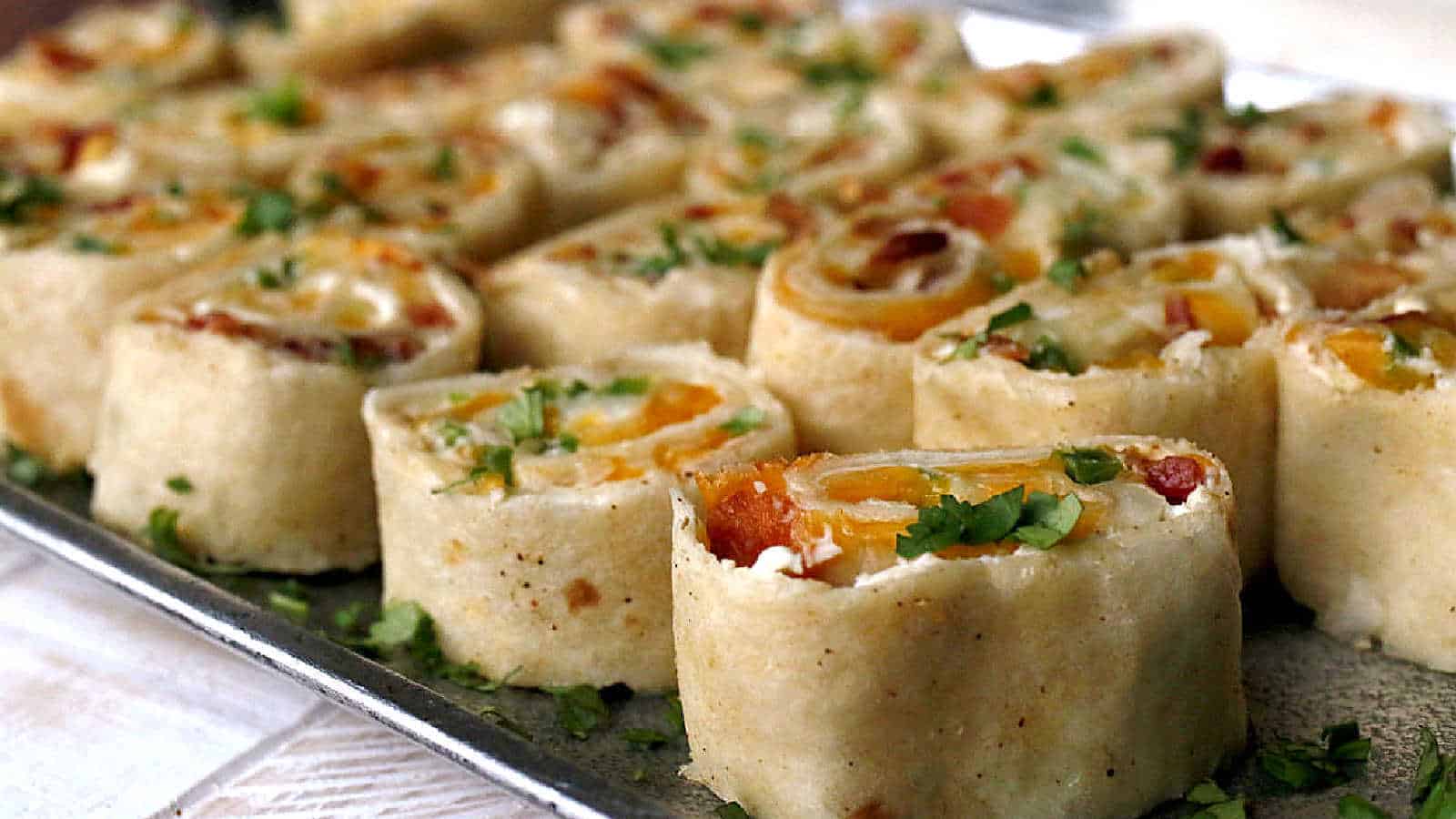 Close-up of sliced tortilla roll-ups filled with cheese, diced vegetables, and herbs on a tray. These new recipes are garnished with chopped cilantro, perfect for those seeking their next favorite recipes.