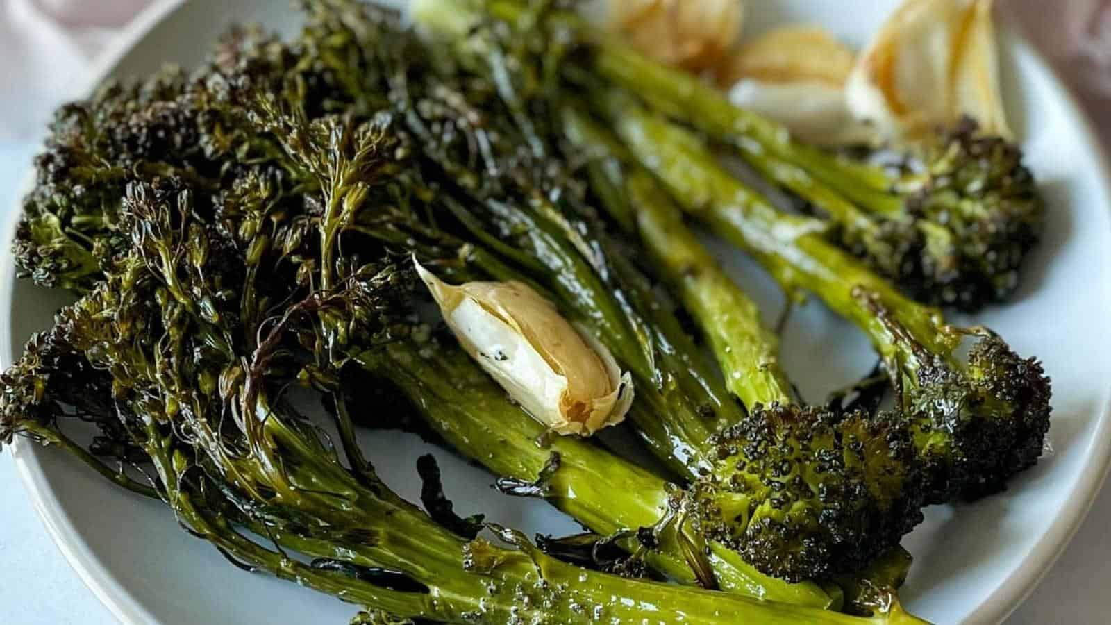 A plate of roasted broccolini and garlic cloves, slightly charred, graces a white dish—a perfect side dish for holiday feasts. The broccolini glistens with oil, and the garlic looks expertly roasted alongside it, promising better feasts ahead.