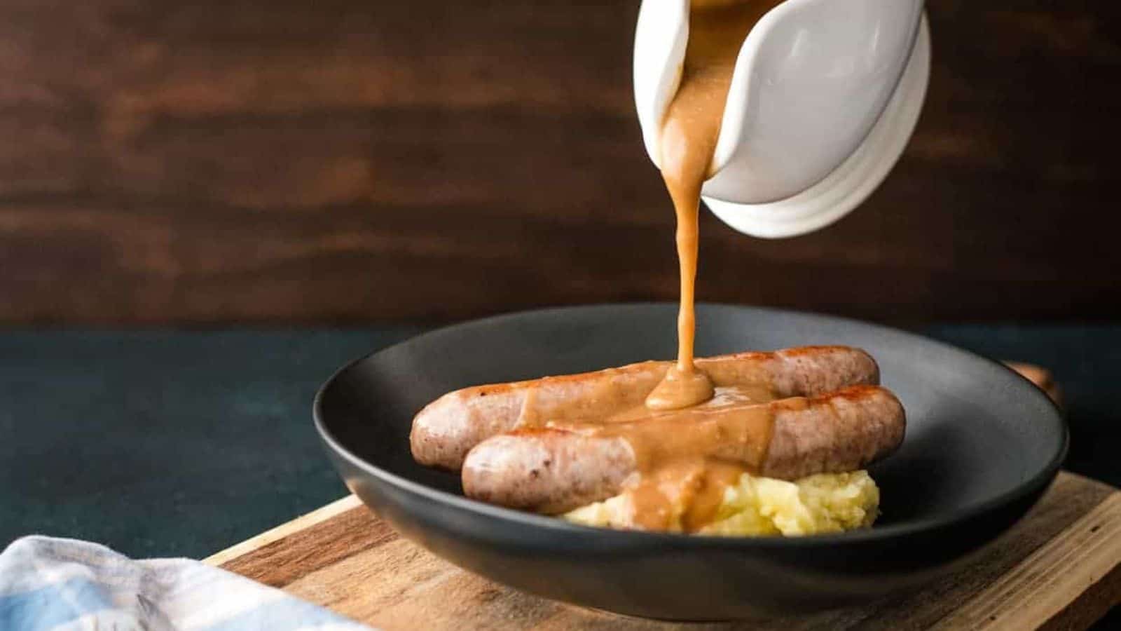 Gravy being poured over sausages and mashed potatoes.