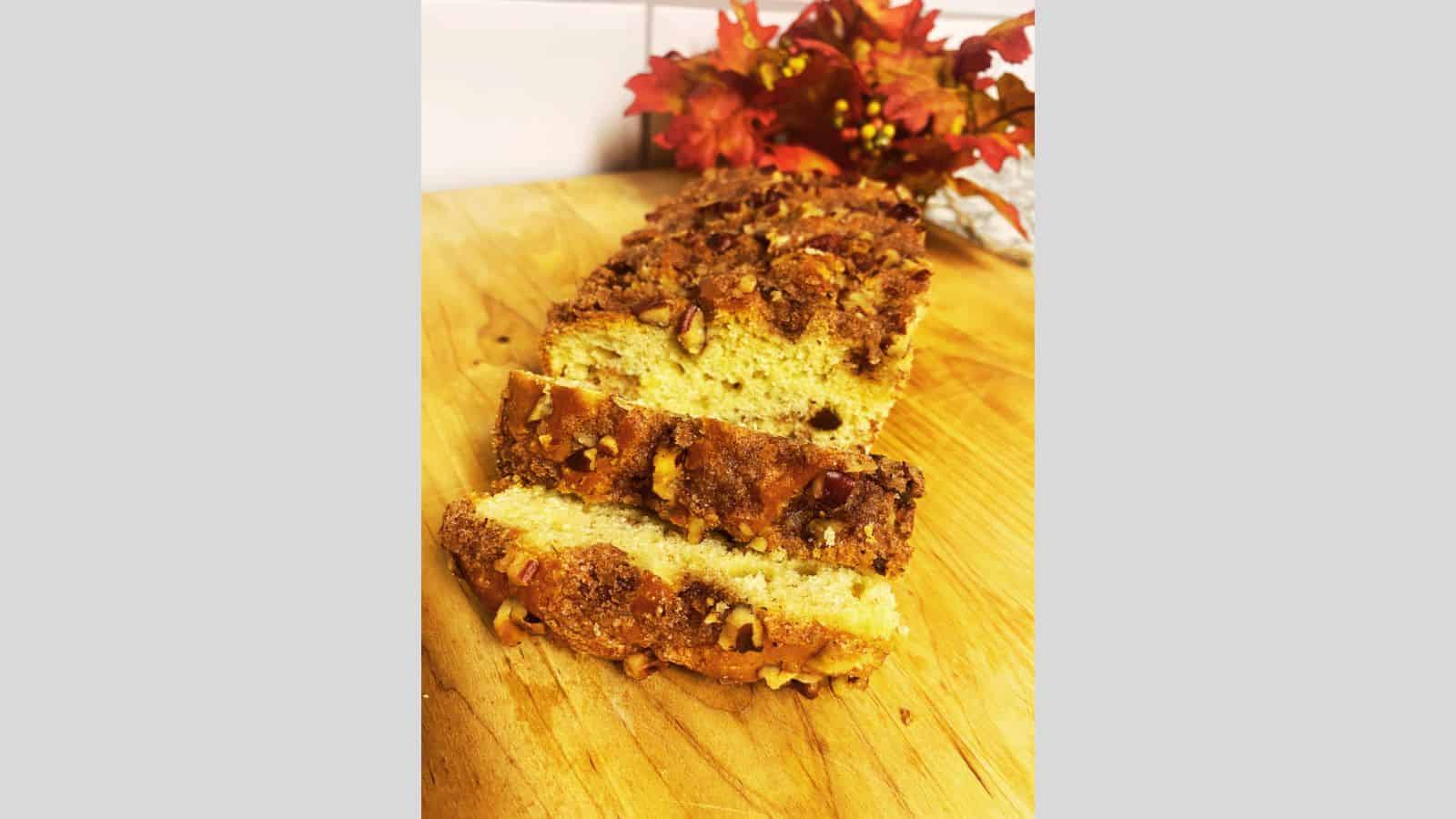 A sliced loaf of wonder bread rests on a wooden cutting board, topped with a brown crumbly mixture and nuts. In the background, red and orange autumn leaves add to the magical setting.