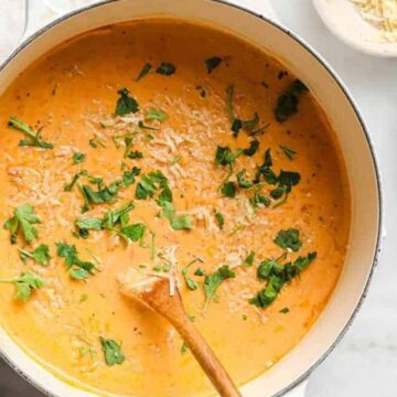Creamy Italian sausage soup in a pot with a spoon and garnishes on the side.