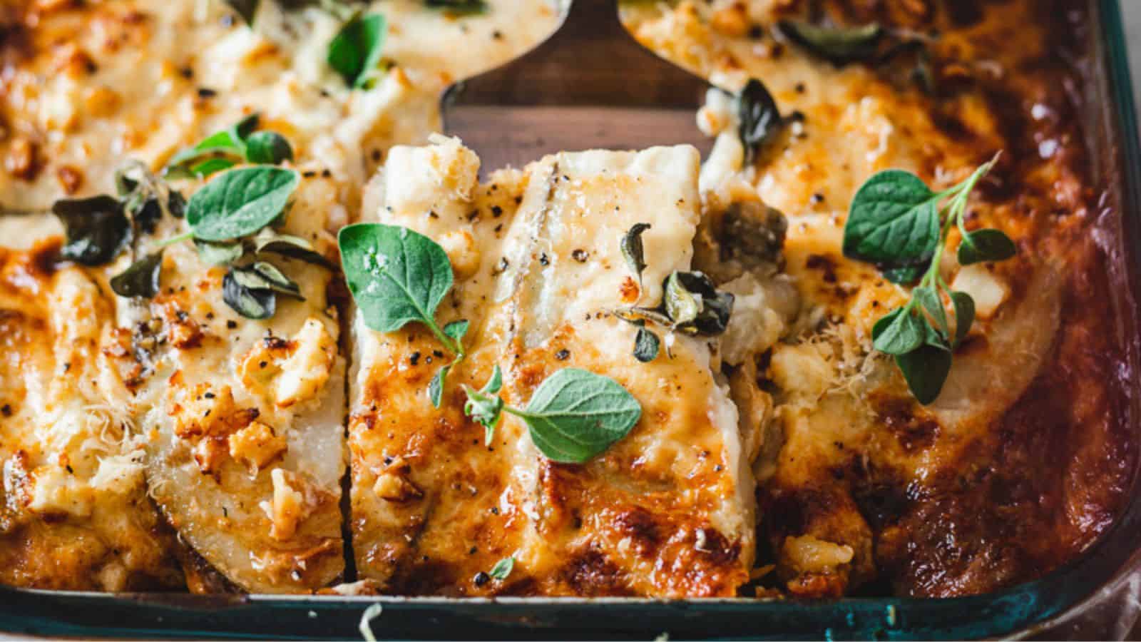 Close-up of a baked casserole dish featuring layers of cheese with crispy golden edges, topped with fresh green herbs.