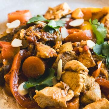 A plate of stir-fried chicken with vegetables, including carrots and bell peppers. The dish is garnished with sliced almonds and fresh cilantro. A fork is placed on the side of the plate.